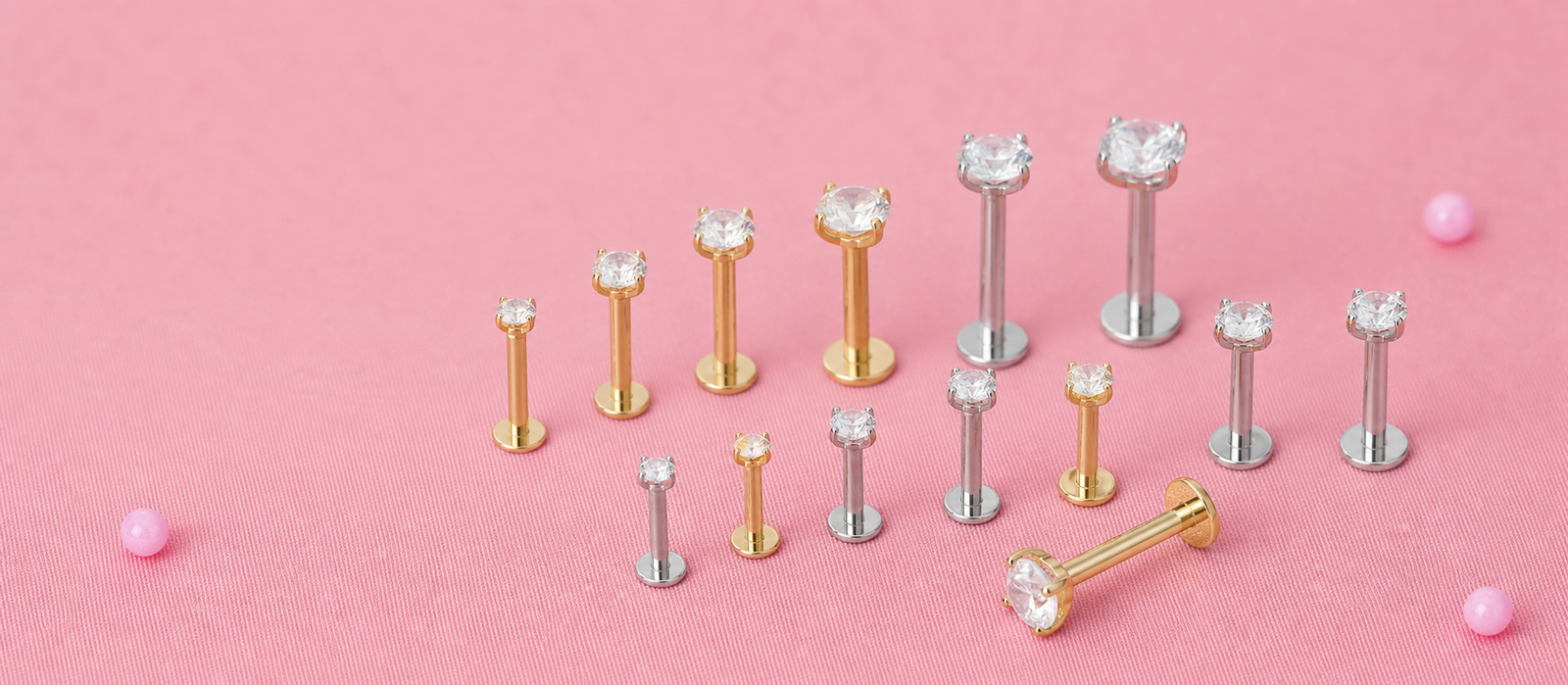 Gold and silver basic round CZ flat back labret studs displayed by size on a soft pink surface