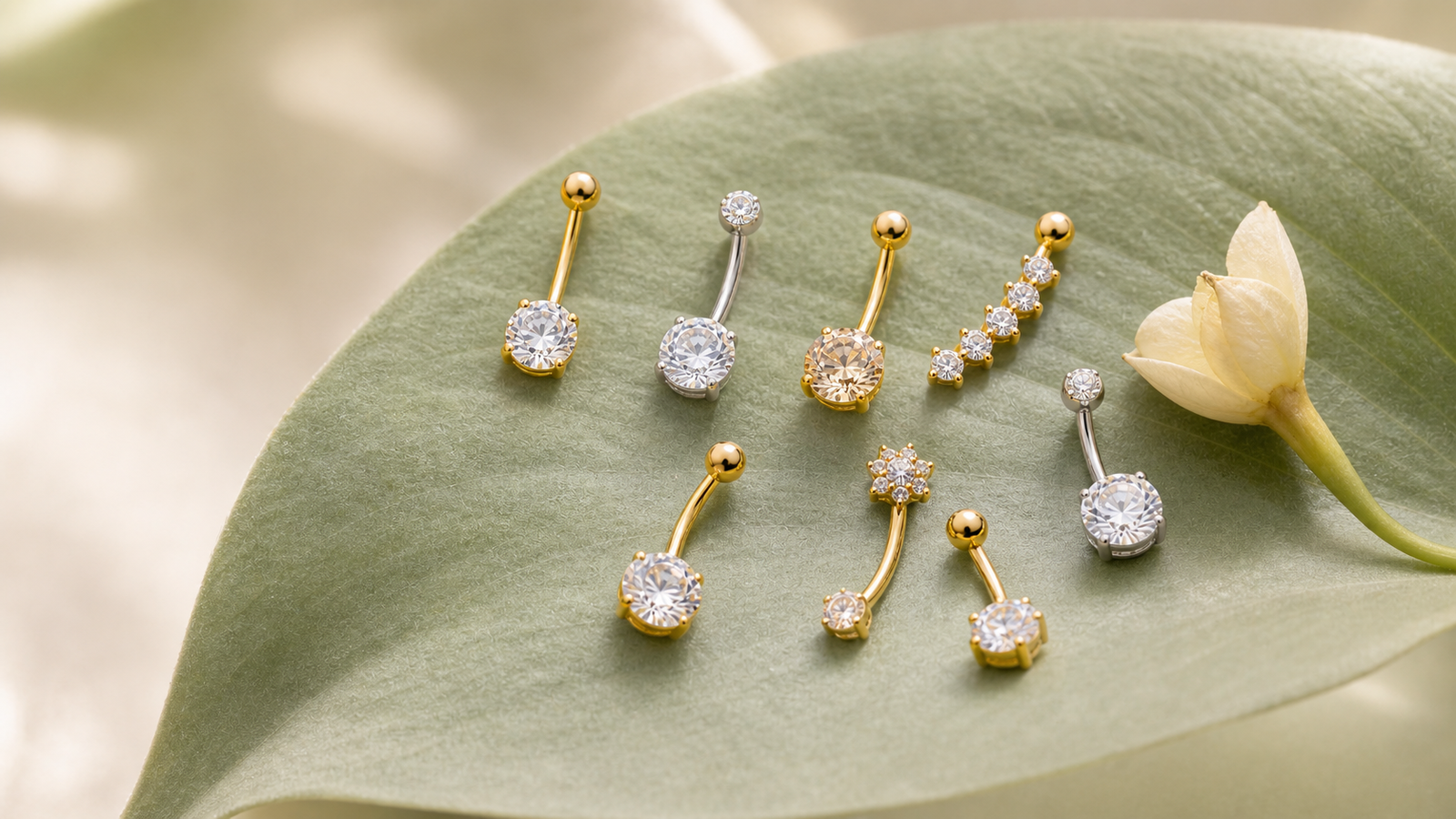 Gold and silver navel jewelry arranged naturally on a soft sage leaf