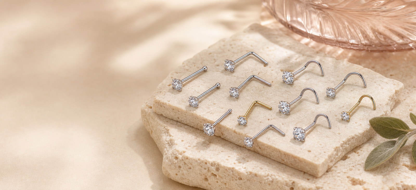 Silver and gold F136 titanium CZ nose studs arranged on warm ivory stone