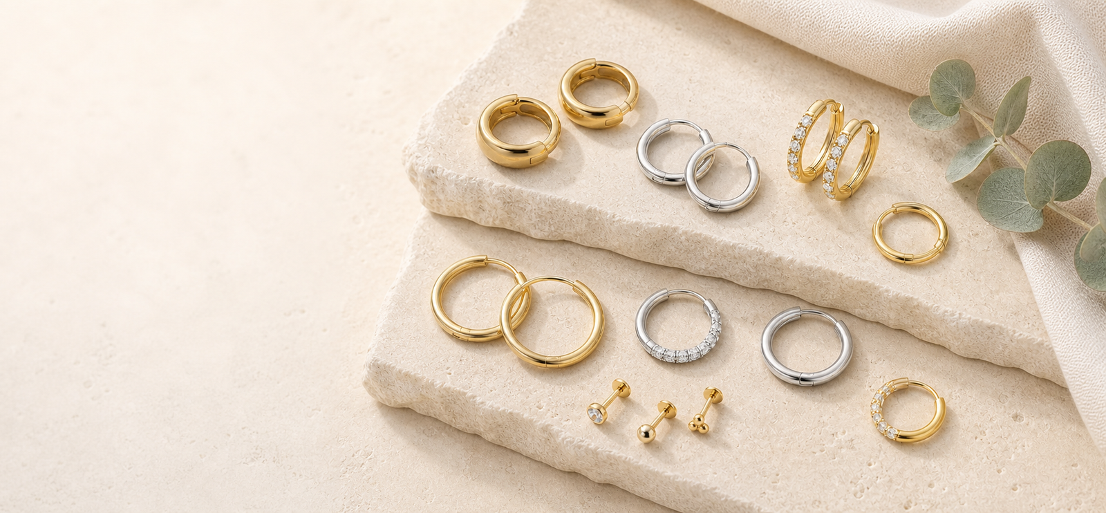 Gold and silver titanium hoop earrings and flat back studs arranged on pale stone