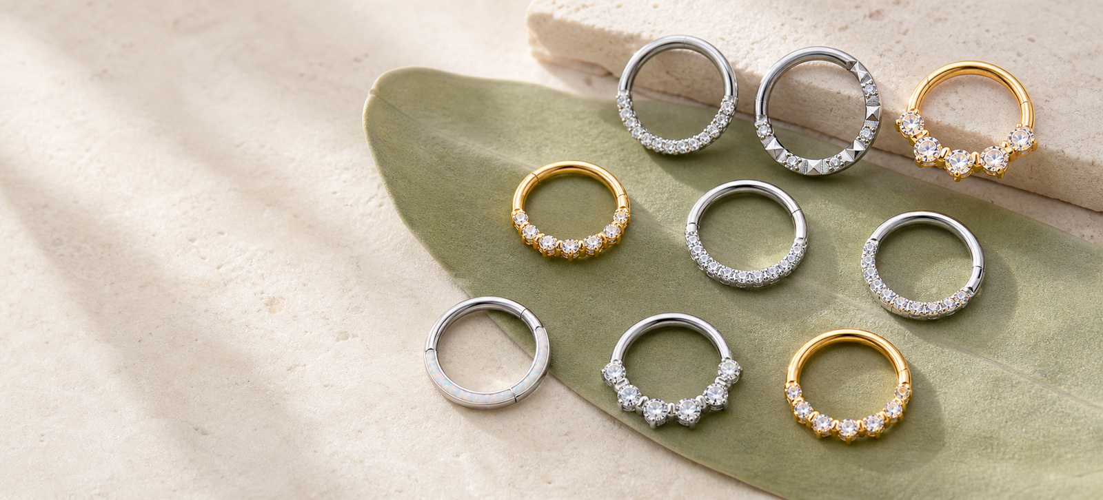 Gold and silver F136 titanium nose rings arranged on a muted sage leaf